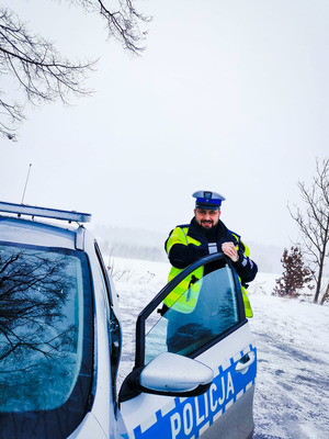 Umundurowany policjant ruchu drogowego stojący przy radiowozie