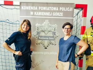 pracownik cywilny oraz umundurowana policjanta przy banerze Komendy Powiatowej POlicji w Kamiennej Górze