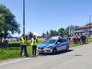 dwóch umundurowanych policjantów polskich stojących przy oznakowanym radiowozie