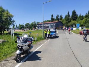 policyjny oznakowany motor, a za nim dwóch umundurowanych policjantów stojących przy oznakowanym radiowozie