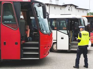 Umundurowany policjant ruchu drogowego piszący w notatniku, w tle dwa autobusy