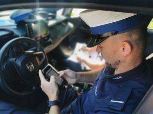 Umundurowany policjant ruchu drogowego siedzi na fotelu kierowcy w radiowozie i dokonuje sprawdzenia na mobilnym terminalu