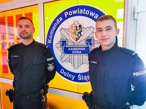 Dwóch umundurowanych policjantów na tle loga kamiennogórskiej komendy