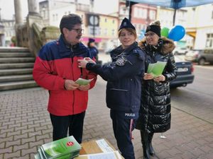 Mężczyzna w czerwonej kurtce, któremu policjantka przypina do kurtki białą wstążkę