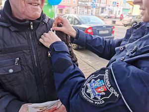 Policjantka przypina białą wstążkę meżczyźnie w czarnej kurtce