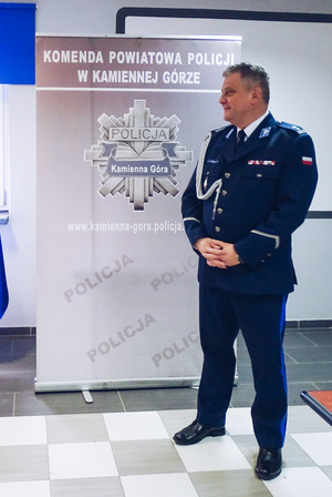 Komendant Powiatowy Policji w Kamiennej Górze w umundurowaniu wyjściowym na tle baneru z napisem Komenda Powiatowa Policji w Kamiennej Górze