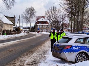 Trzech umundurowanych policjantów stojących przy oznakowanym radiowozie