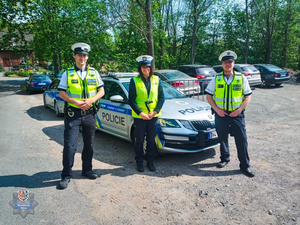 Dwóch policjantów policji czeskiej, i policjantka ruchu drogowego, stojący przy oznakowanym radiowozie czeskiej policji