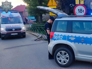 Na zdjęciu radiowóz, przy którym stoi policjant, w tle karetka pogotowia i na jezdni leży rower