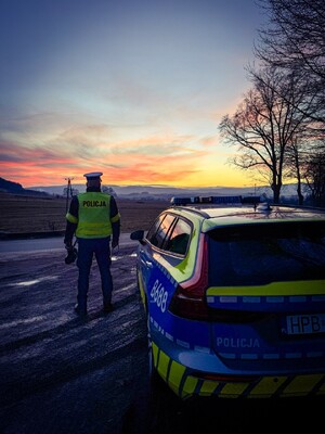 Policjant stojący przy radiowozie podczas zachodu słońca
