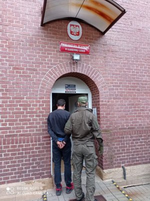 policjant wydziału kryminalnego doprowadza do Prokuratury zatrzymanego mężczyzne z założonymi kajdankami